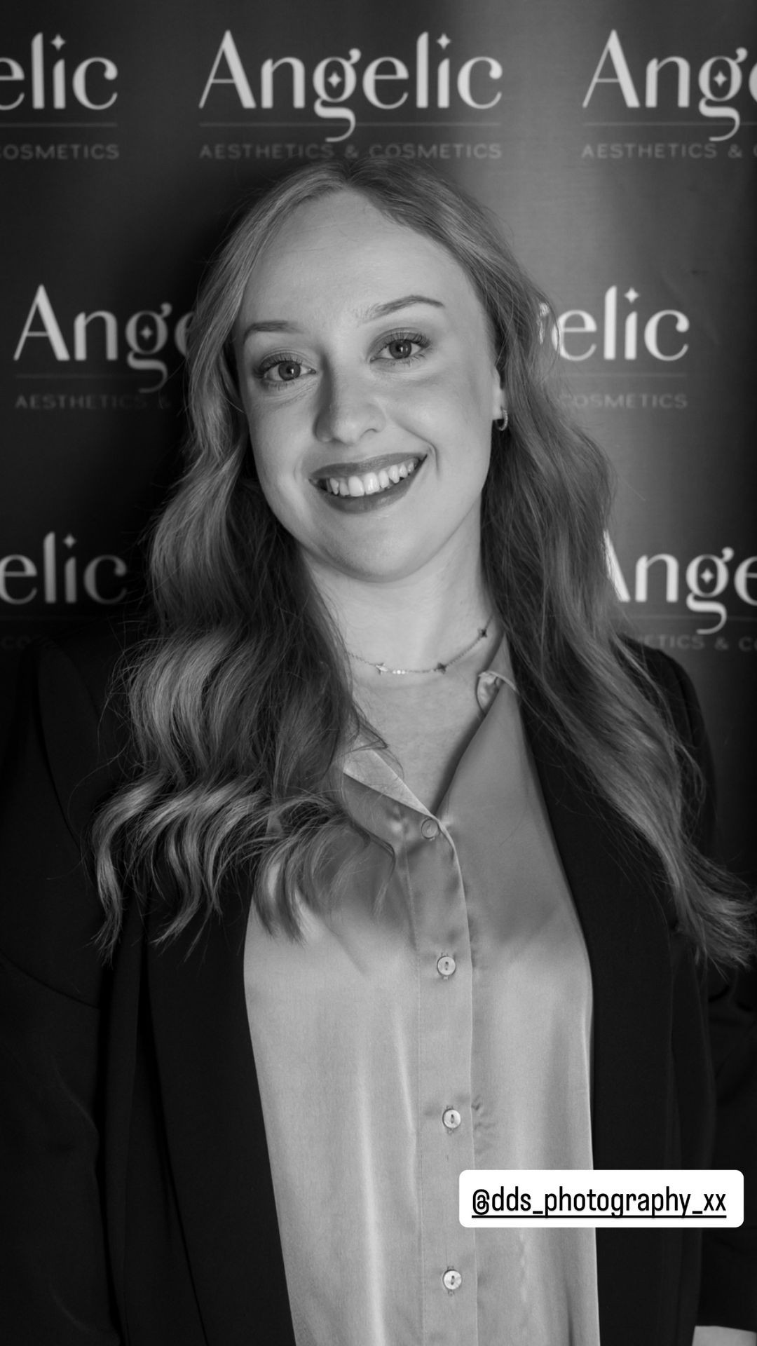 Smiling person with wavy hair at an Angelic Aesthetics event backdrop.